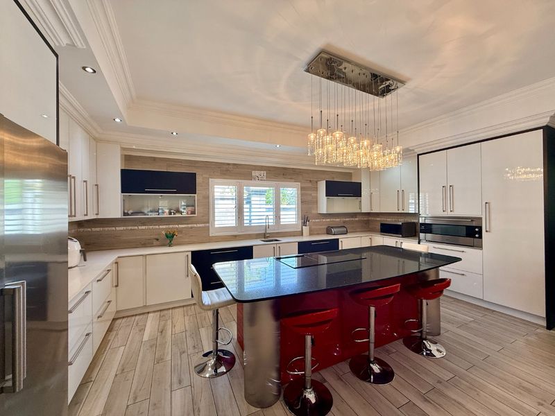 Modern kitchen featuring a large central island with a breakfast bar, high-gloss cabinetry, integrated appliances, and elegant pendant lighting.
