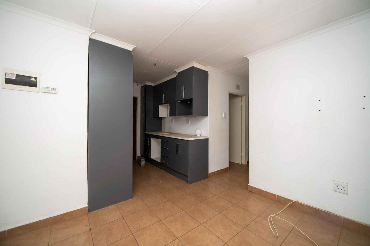 A compact kitchen area featuring dark grey cabinetry, tiled flooring, and neutral walls, currently awaiting final appliance installation and finishing touches.