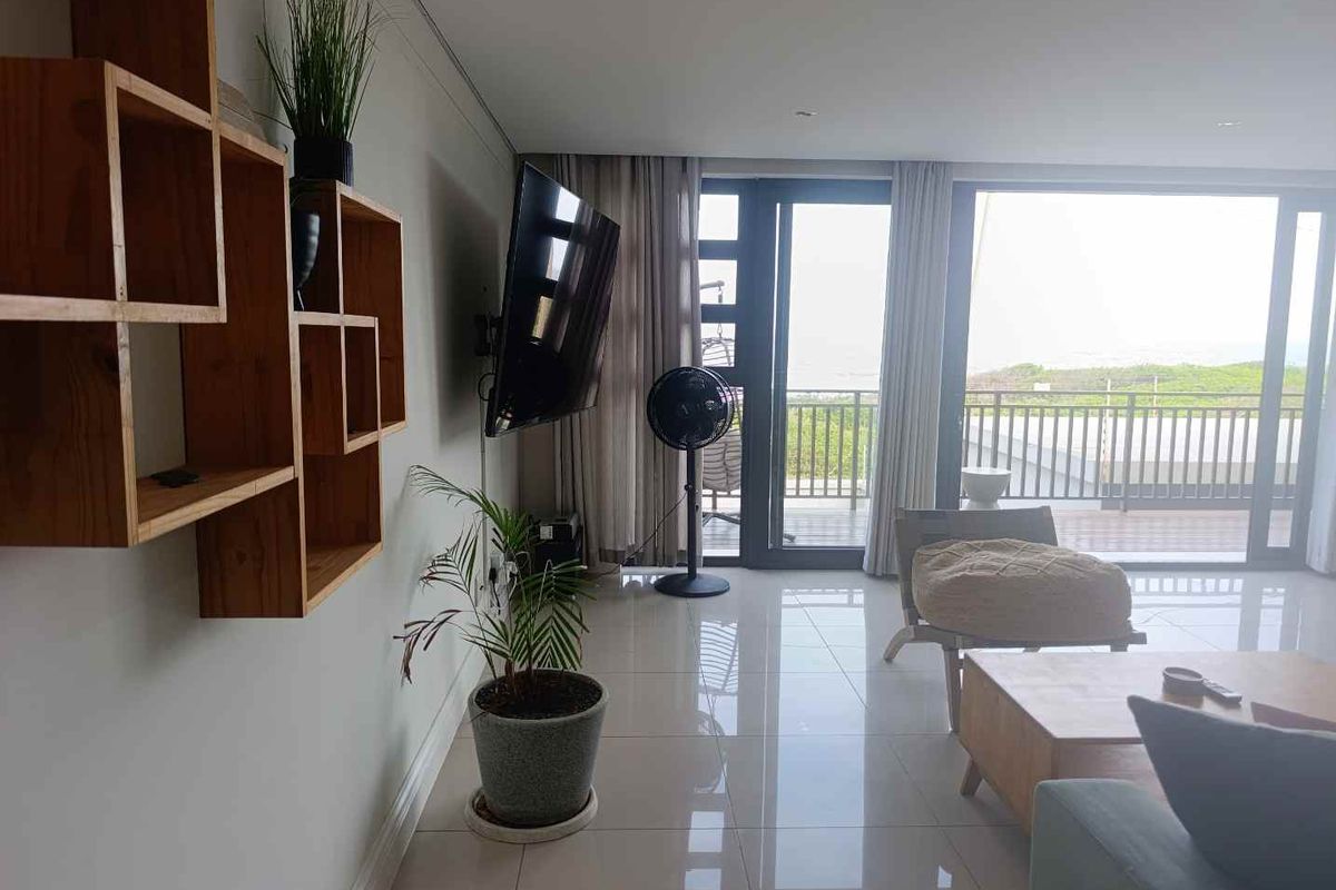 Modern living room featuring polished porcelain floor tiles, recessed lighting, and large sliding glass doors providing access to a balcony with coastal views.