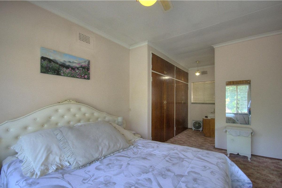 A bedroom featuring built-in wooden wardrobes, carpeted flooring, and a ceiling fan, offering a functional and traditional layout.