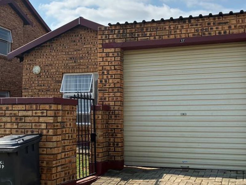 Front view of a face-brick cluster home featuring a single garage, paved driveway, and secure gated entrance.