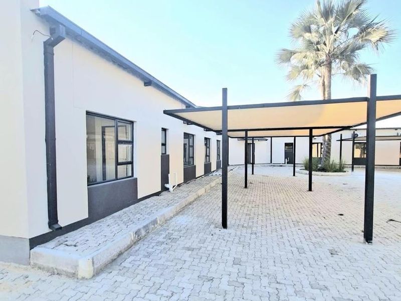 Exterior view of the office building featuring a paved parking area with a modern shade sail structure and aluminium-framed windows.
