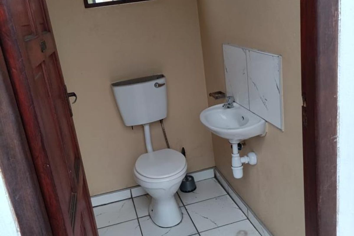 A compact guest bathroom featuring a toilet, wall-mounted basin, and tiled flooring, requiring minor cosmetic updates to improve its overall condition.