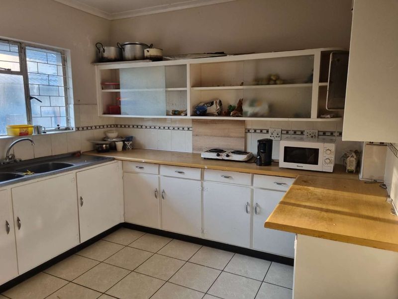 A functional kitchen featuring white cabinetry, laminate countertops, tiled flooring, and a stainless steel sink, offering potential for modern renovation and aesthetic updates.