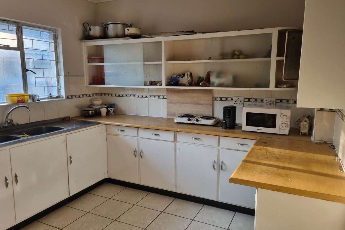 A functional kitchen featuring white cabinetry, laminate countertops, tiled flooring, and a stainless steel sink, offering potential for modern renovation and aesthetic updates.