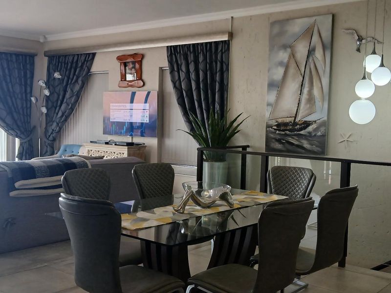 Spacious open-plan living and dining area featuring large glass sliding doors with ocean views, tiled flooring, and a modern textured feature wall.