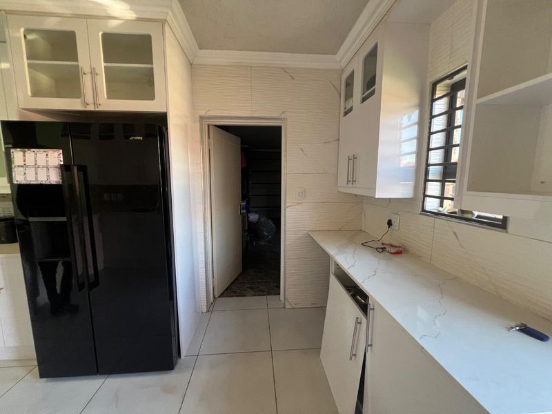 A kitchen featuring white cabinetry, stone countertops, and textured wall tiles, with a doorway leading to an adjacent utility or storage space.