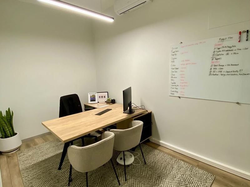 A modern, well-lit office space featuring laminate flooring, a wall-mounted whiteboard, and a split-system air conditioning unit.