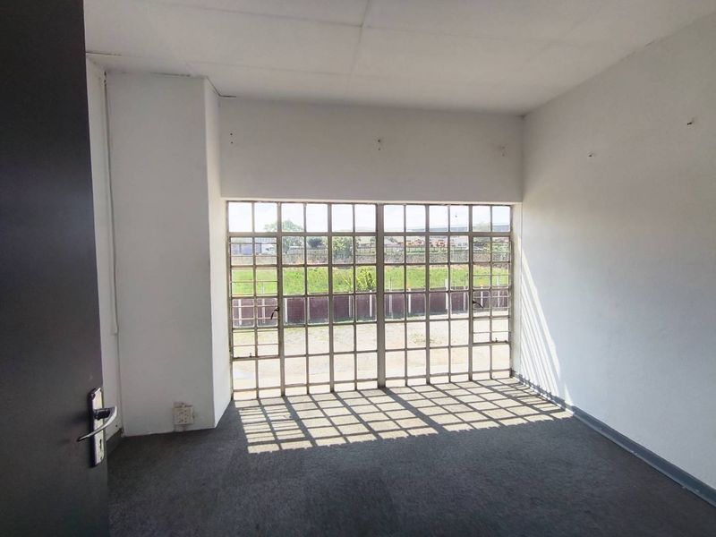 An empty office space featuring carpet flooring, a drop ceiling, and large windows with security bars, offering natural light and a functional layout.