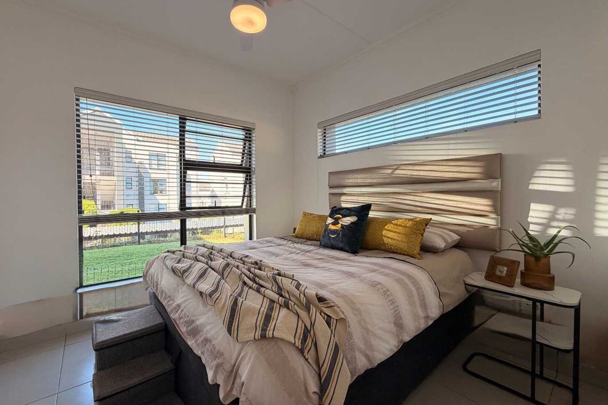 A bright and well-maintained bedroom featuring tiled flooring, a ceiling fan, and dual-aspect windows with fitted horizontal blinds.