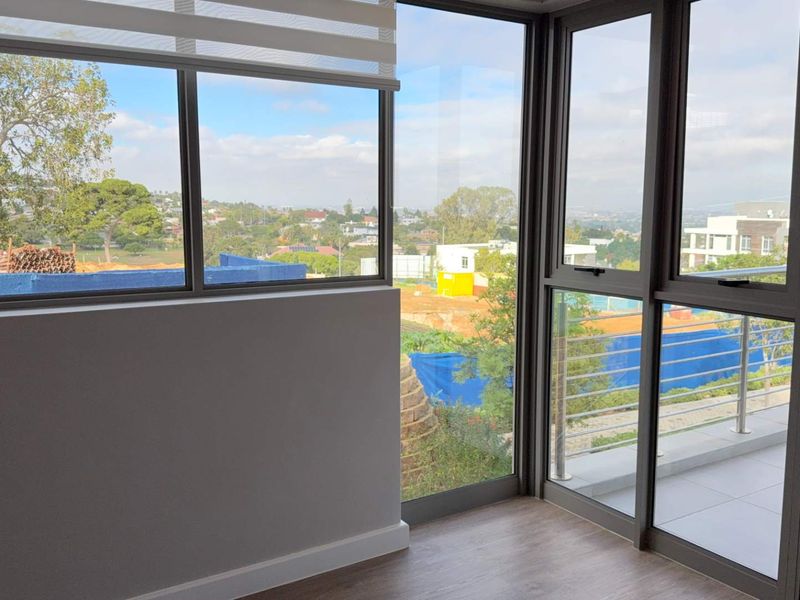 Bright and modern living area featuring expansive floor-to-ceiling windows, laminate flooring, and direct access to an outdoor balcony with scenic views.