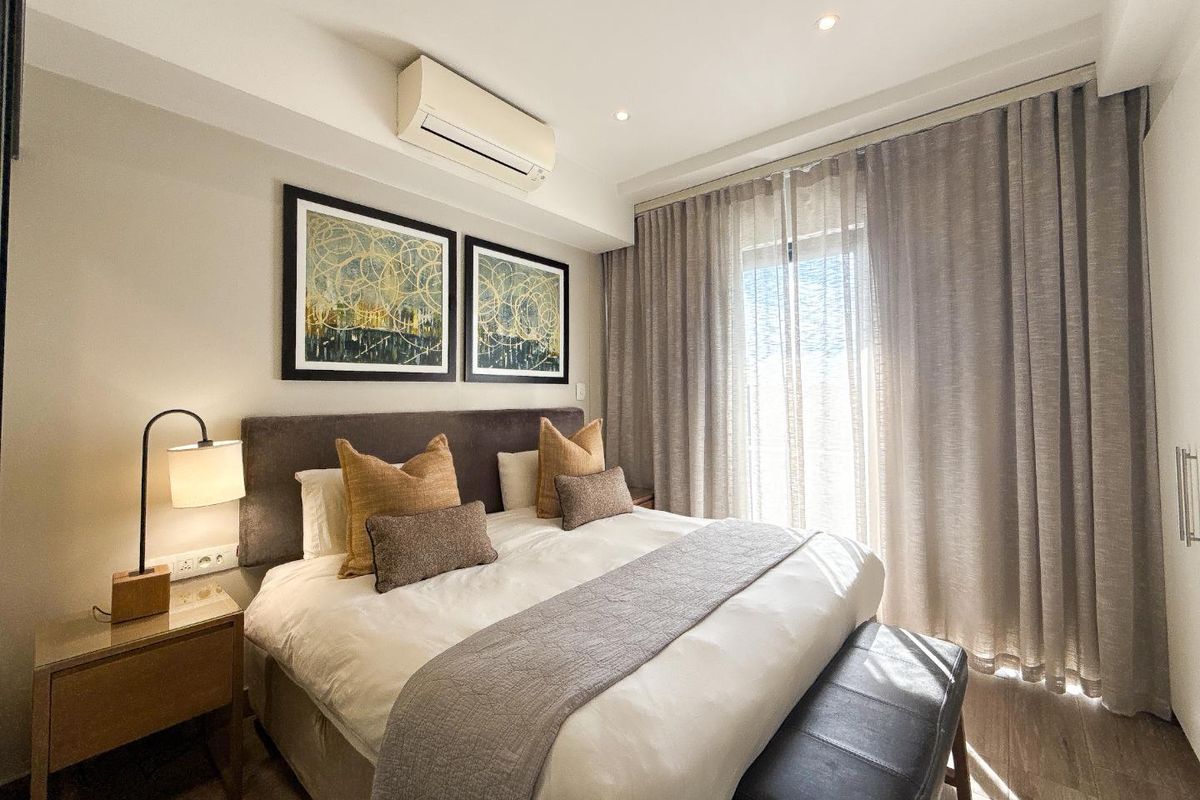 A well-maintained bedroom featuring laminate flooring, recessed downlighting, a wall-mounted split-system air conditioner, and a built-in wardrobe.