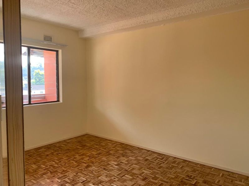 An empty bedroom featuring classic parquet flooring, a textured ceiling, and a window providing natural light.