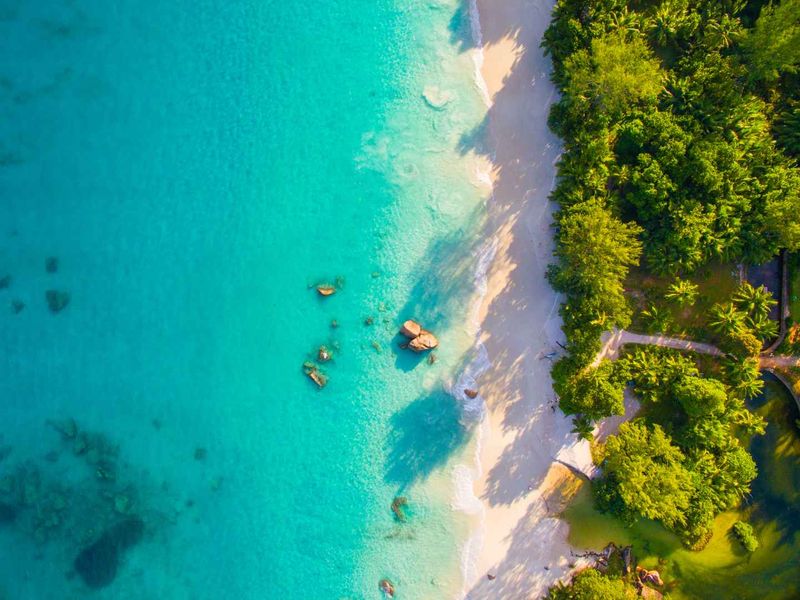 An aerial view of a pristine tropical coastline featuring turquoise waters, white sandy beach, and lush coastal vegetation.