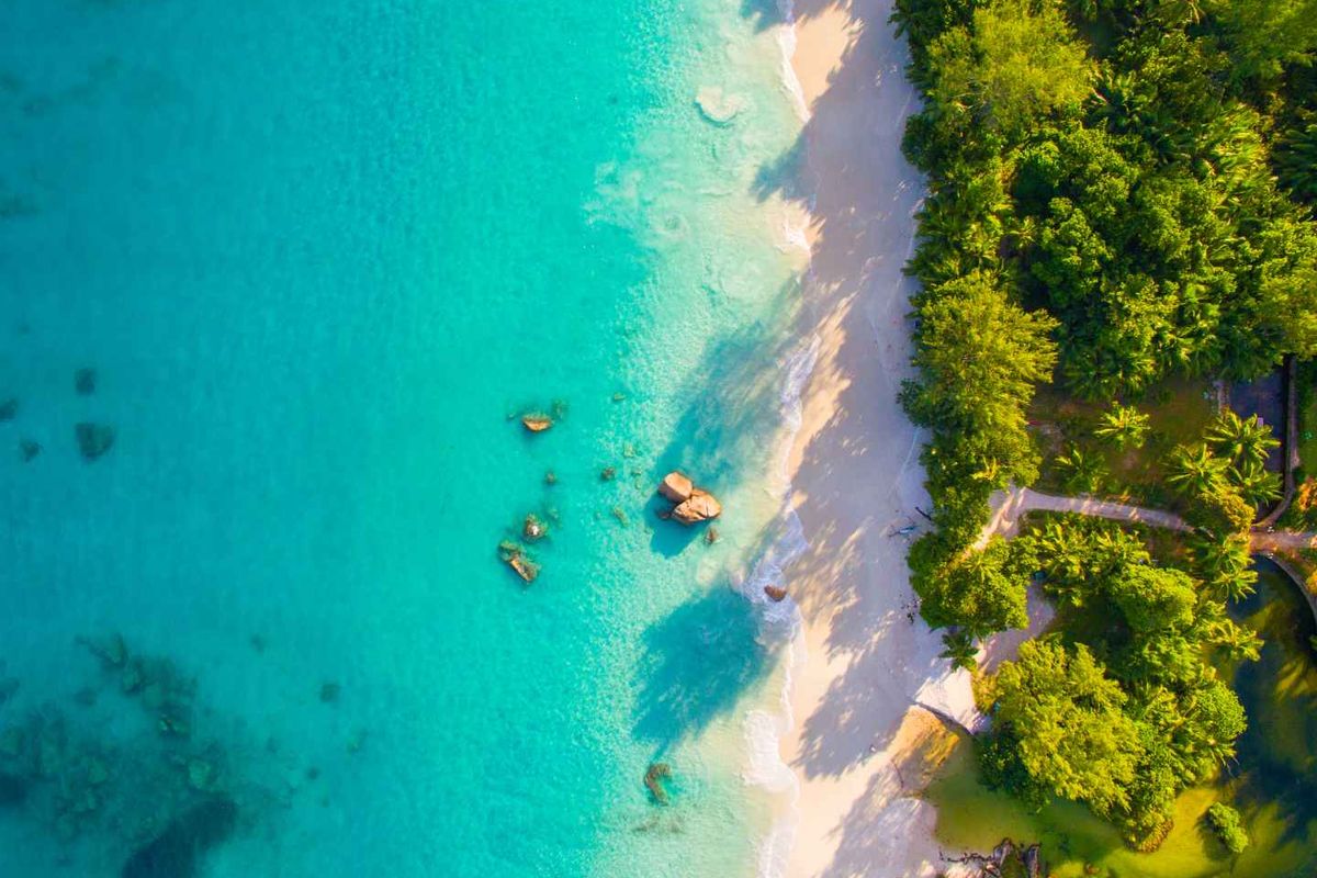 An aerial view of a pristine tropical coastline featuring turquoise waters, white sandy beach, and lush coastal vegetation.