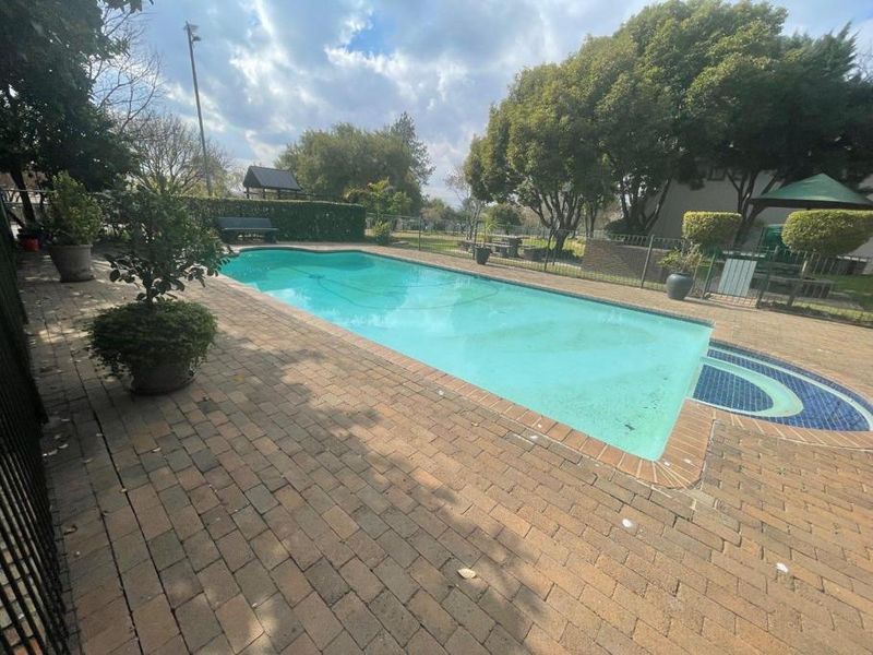 Outdoor swimming pool area featuring brick paving, metal perimeter fencing, and established garden surroundings.
