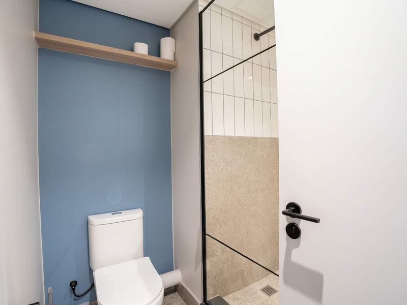 Modern bathroom featuring a walk-in shower with black frame, terrazzo-style flooring, and a blue accent wall with a floating shelf.