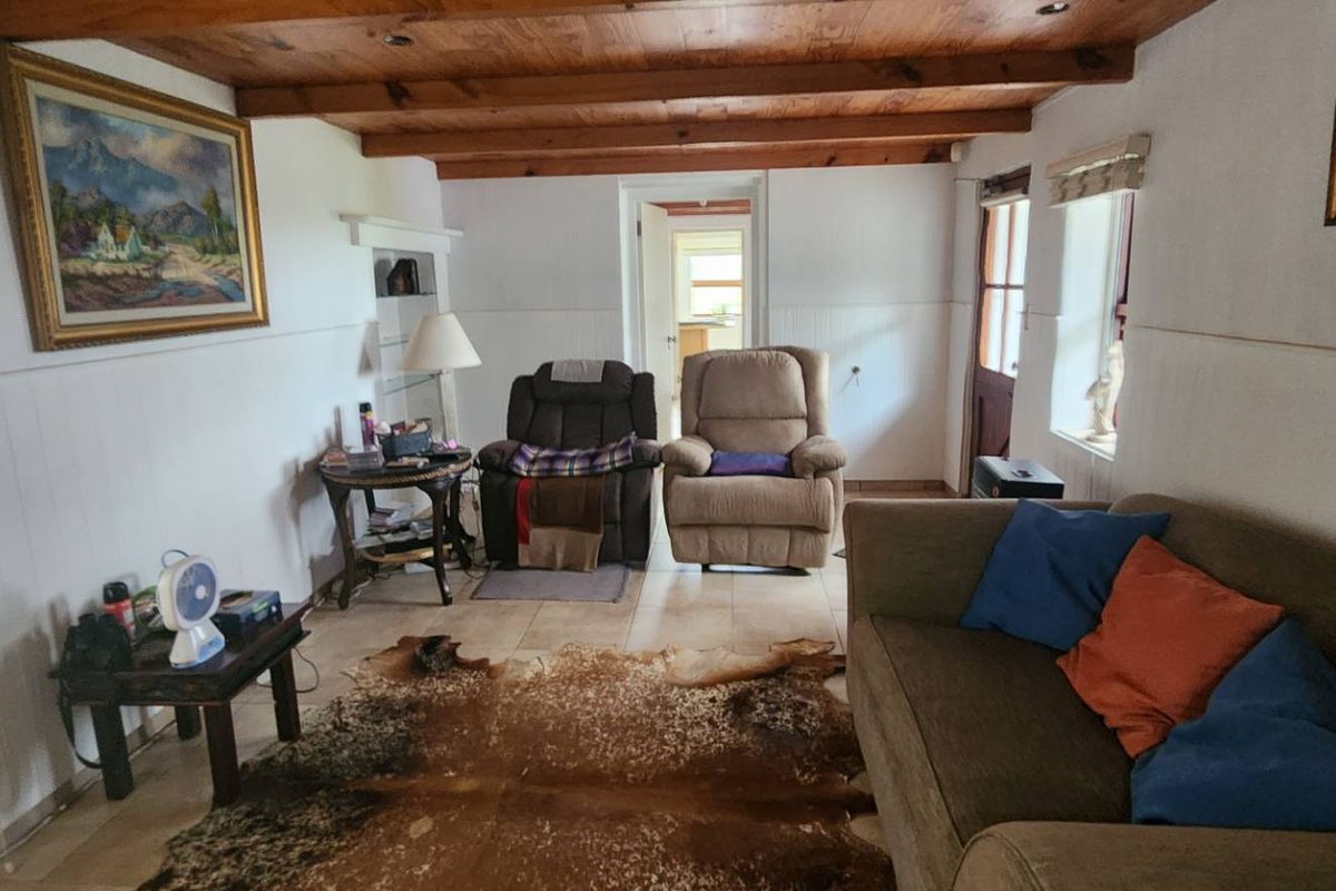 A cozy living room featuring exposed timber ceiling beams, tiled flooring, and built-in shelving, offering a rustic farm-style aesthetic.