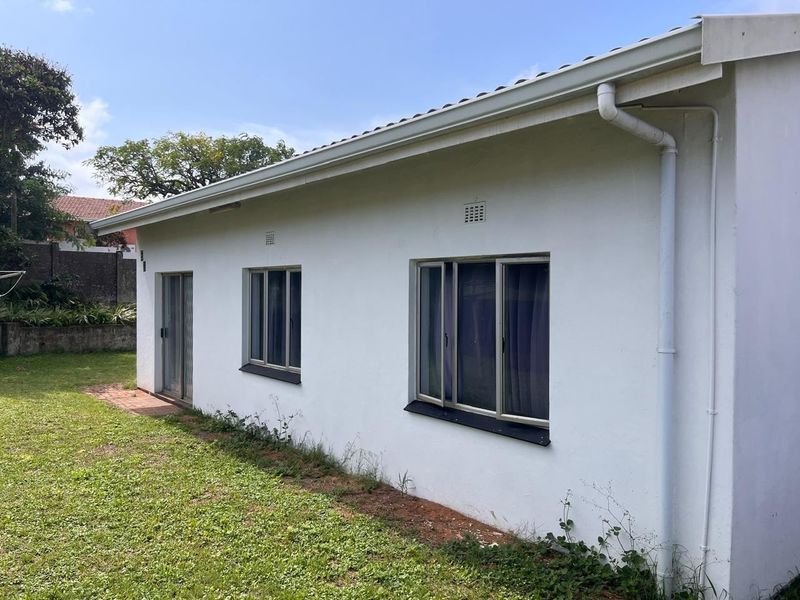 Rear exterior view of the property featuring white rendered walls, aluminium window frames, a sliding door, and functional guttering system.