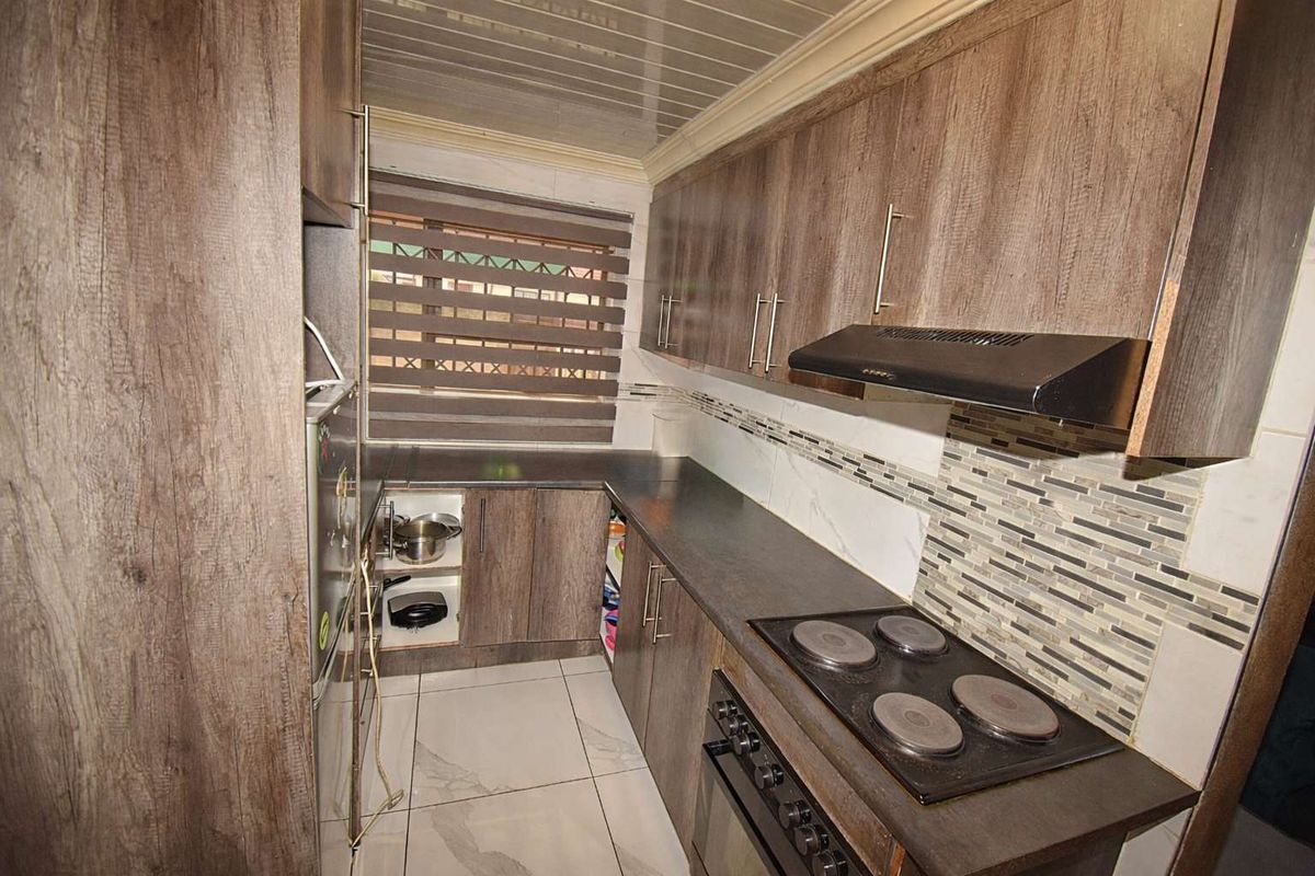Compact kitchen featuring wood-look cabinetry, dark laminate countertops, a built-in electric hob, extractor fan, and tiled flooring with a mosaic backsplash.