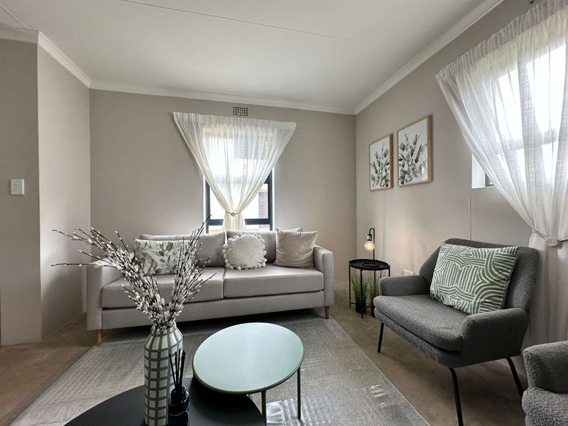 A well-maintained living room featuring neutral wall tones, coving, and natural light through two windows.