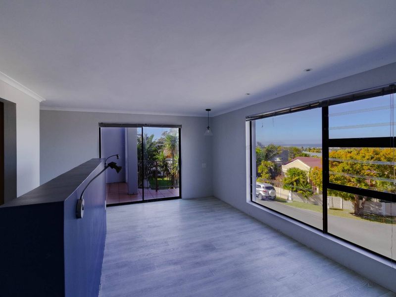 Bright and spacious living area featuring modern laminate flooring, large windows with neighborhood views, and access to an outdoor balcony.