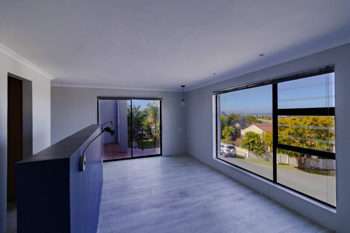 Bright and spacious living area featuring modern laminate flooring, large windows with neighborhood views, and access to an outdoor balcony.