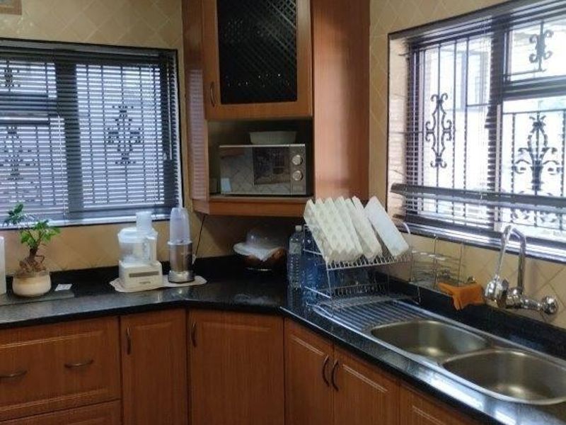 A functional kitchen featuring wood-finish cabinetry, granite countertops, a double stainless steel sink, and tiled flooring with security bars on the windows.