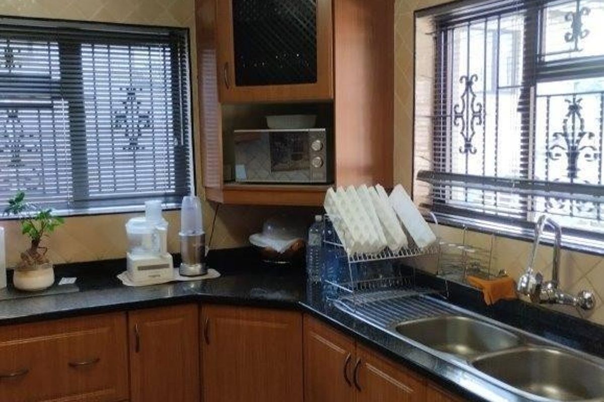 A functional kitchen featuring wood-finish cabinetry, granite countertops, a double stainless steel sink, and tiled flooring with security bars on the windows.