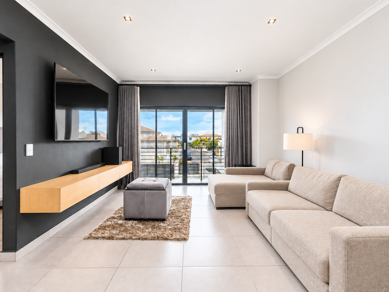 Modern living room featuring tiled floors, a sleek floating media console, and large sliding glass doors opening to a balcony.