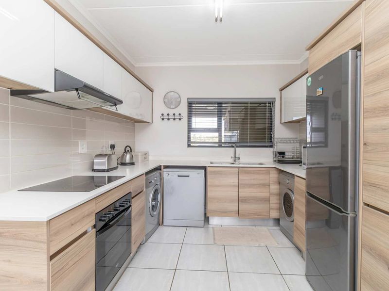 Modern kitchen featuring wood-grain cabinetry, white countertops, integrated appliances, and tiled flooring with a functional layout.