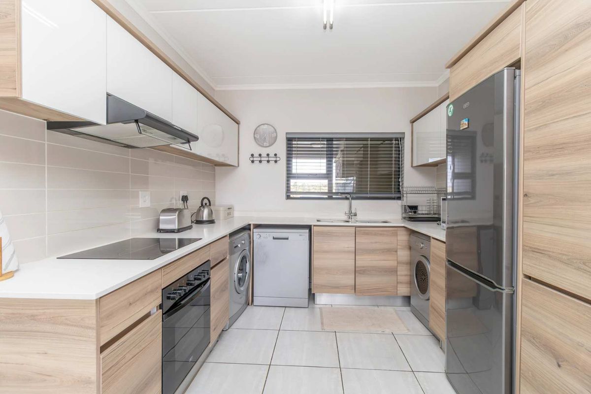 Modern kitchen featuring wood-grain cabinetry, white countertops, integrated appliances, and tiled flooring with a functional layout.