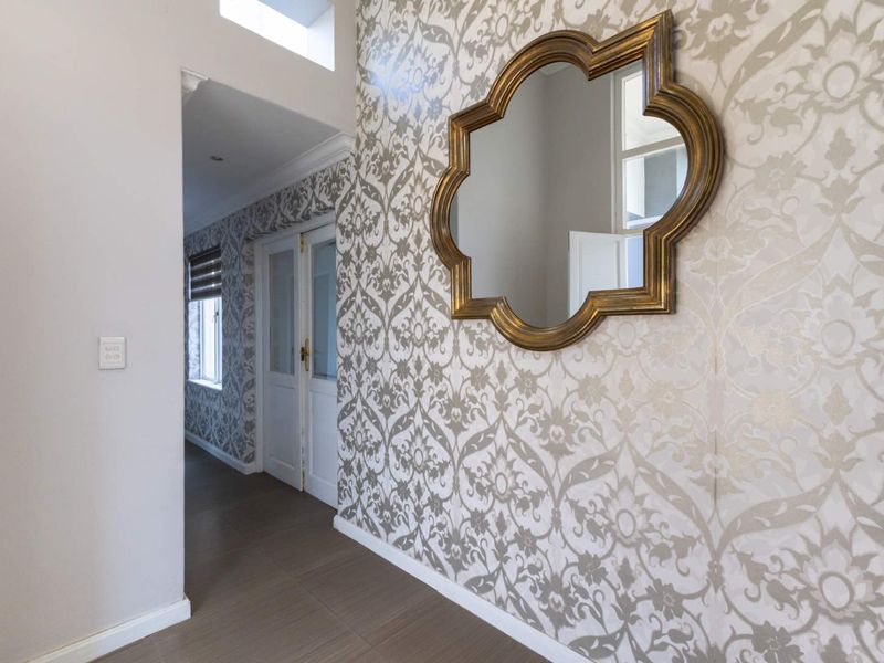 A bright and well-maintained hallway featuring decorative patterned wallpaper, tiled flooring, and a skylight, leading through double glass-panelled doors.