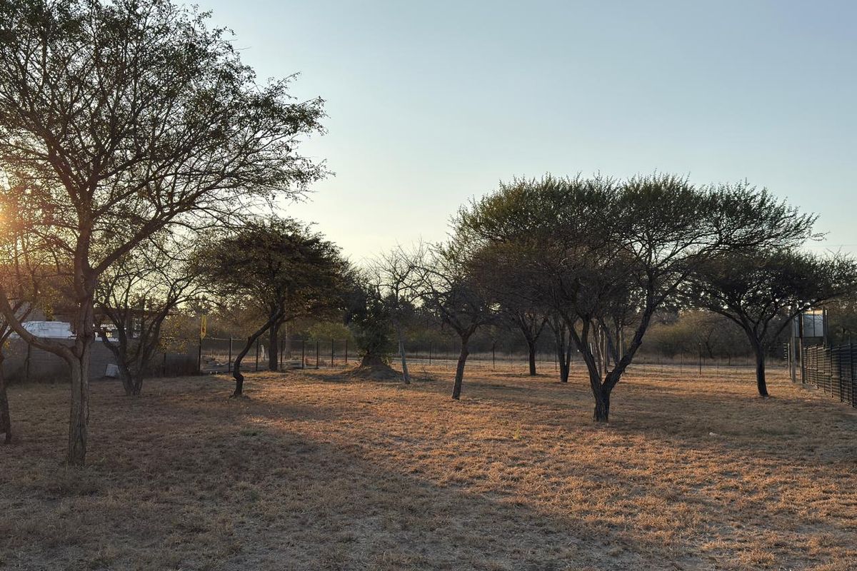 A spacious, open plot of land featuring mature trees and perimeter fencing, offering a natural setting for potential commercial development.