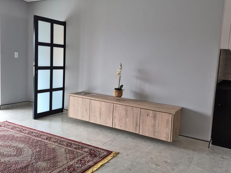 A modern living area featuring neutral grey walls, large format tiled flooring, and a contemporary floating wooden media console.