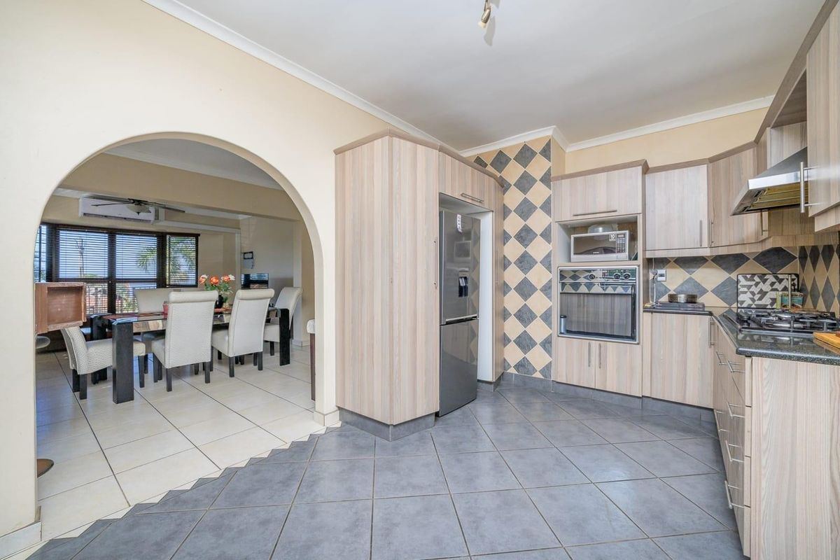 A functional kitchen featuring light wood cabinetry, built-in appliances, and a tiled backsplash, connected to the dining area via a classic archway.