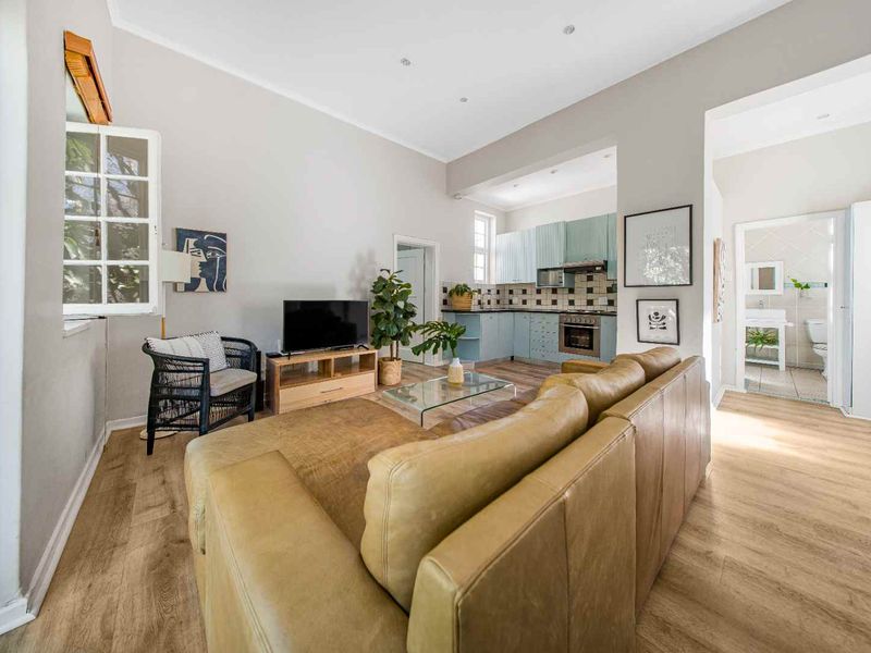 Open-plan living area featuring light laminate flooring, recessed lighting, and a functional kitchen with built-in cabinetry, oven, and extractor fan.