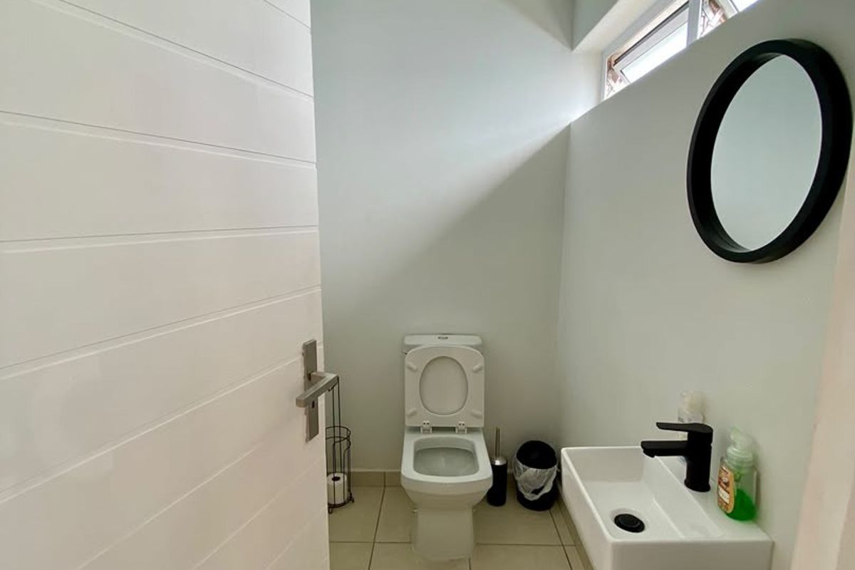 A clean, modern female restroom featuring a wall-mounted basin with black fixtures, a standard toilet, and tiled flooring with natural light from a clerestory window.