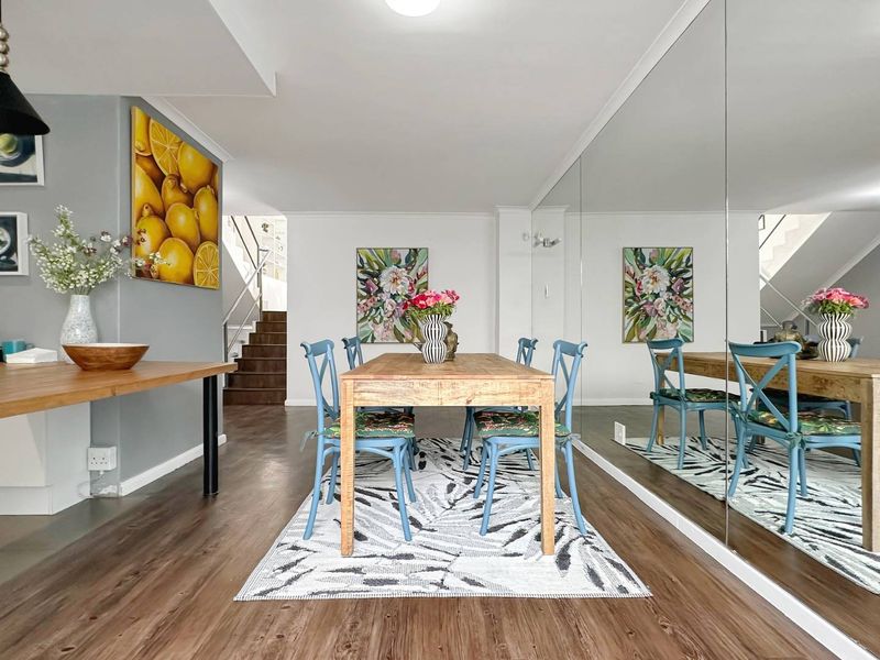 A bright dining area featuring modern laminate flooring, a large feature mirrored wall, and an open-plan layout leading to an internal staircase.