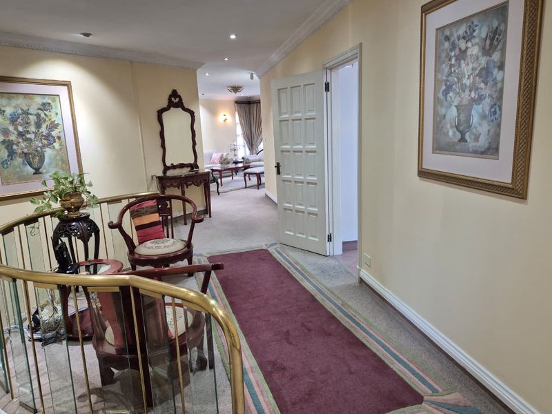 A spacious upper-level hallway featuring a brass balustrade, recessed lighting, and decorative coving, providing access to adjacent living areas.