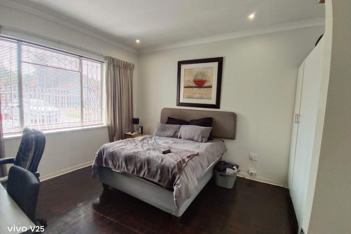 A well-lit bedroom featuring dark hardwood flooring, built-in wardrobe cabinetry, and large windows with fitted blinds.