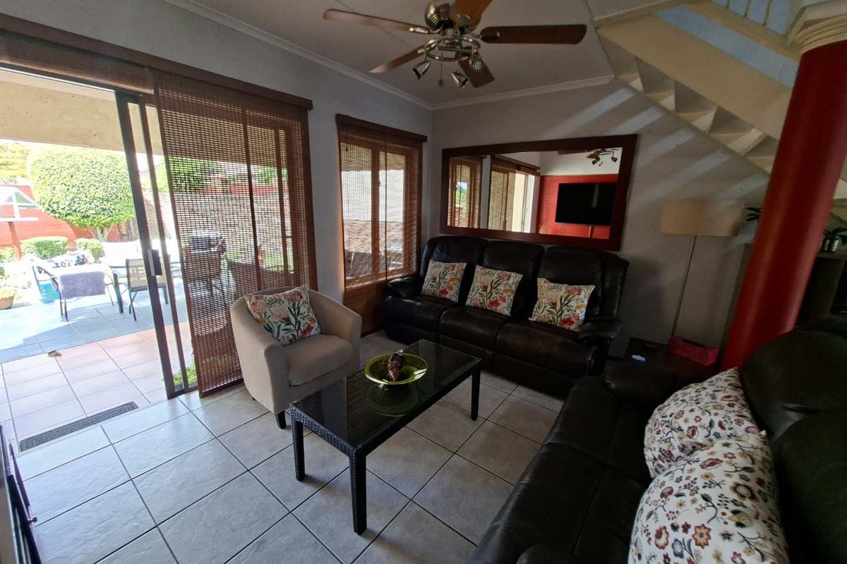 A comfortable living room featuring tiled flooring, a ceiling fan, and large sliding glass doors that provide direct access to the outdoor patio area.
