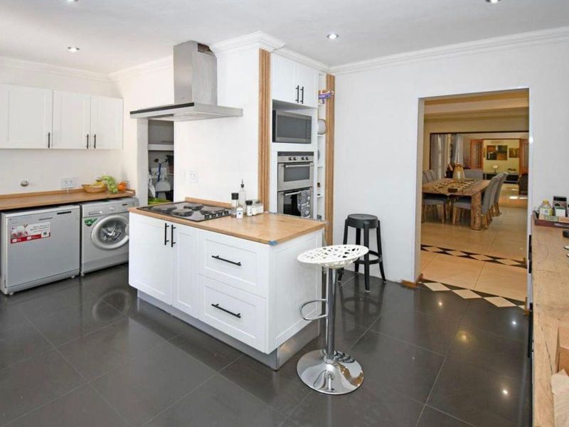 Modern kitchen featuring white cabinetry, wooden countertops, built-in appliances, and a gas hob, with a seamless flow into the adjacent dining area.