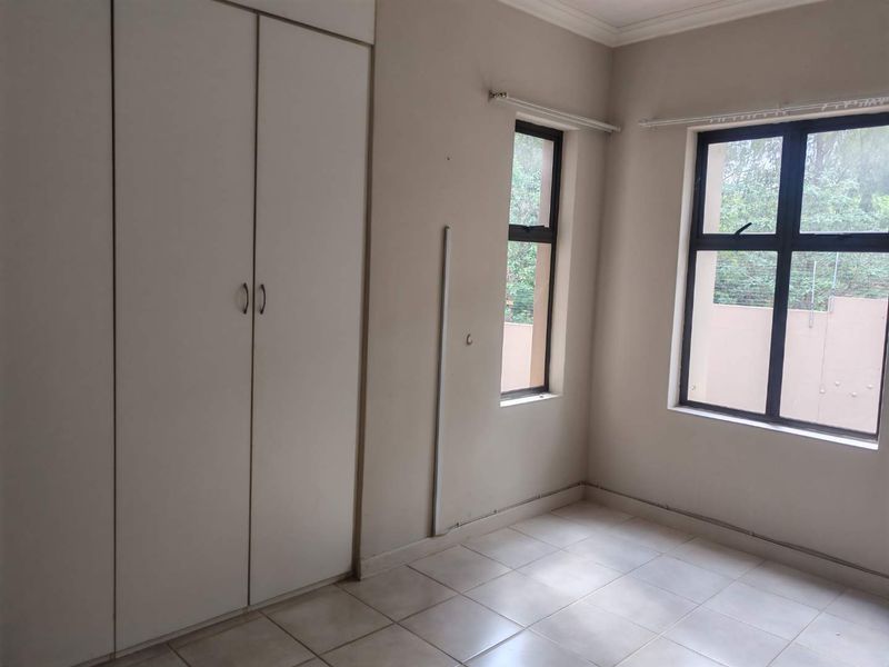 A vacant bedroom featuring tiled flooring, built-in cupboards, and aluminium-framed windows, offering a neutral canvas for personalization.