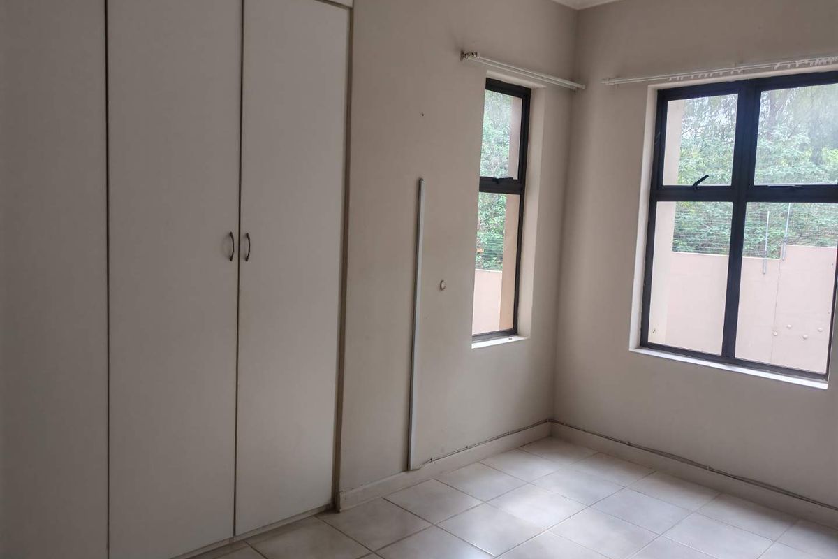 A vacant bedroom featuring tiled flooring, built-in cupboards, and aluminium-framed windows, offering a neutral canvas for personalization.