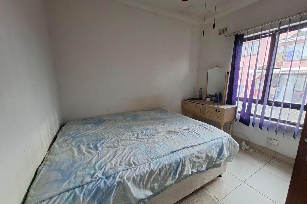 A bedroom featuring tiled flooring, a ceiling fan, and a large window allowing natural light. The space requires cosmetic updates to the walls and ceiling.