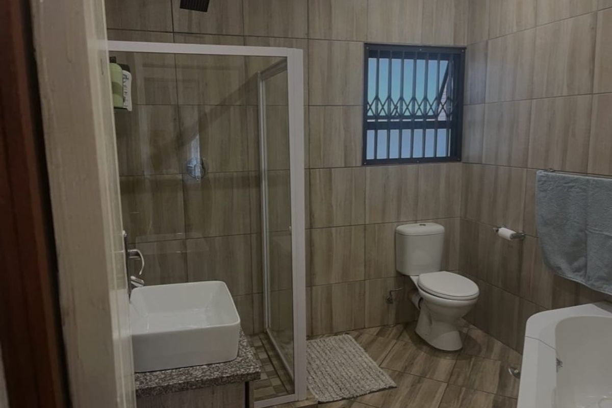 A modern bathroom featuring wood-look floor and wall tiles, a glass-enclosed shower, a vessel sink vanity, and a toilet.