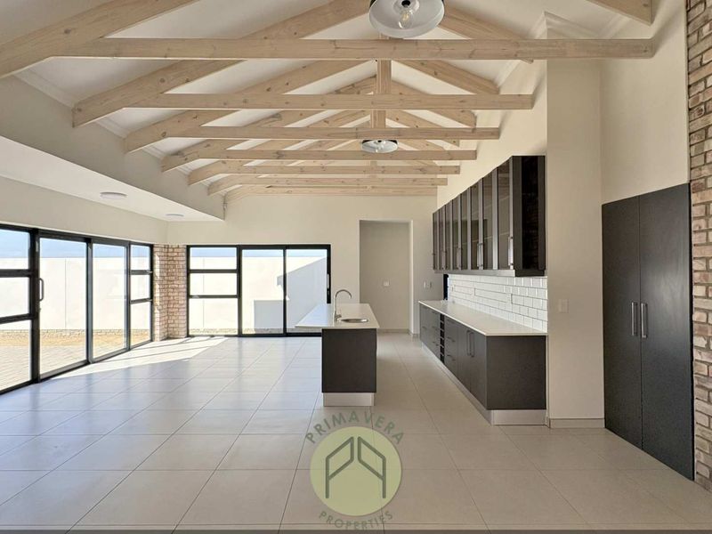 Spacious open-plan living and kitchen area featuring exposed timber trusses, a brick fireplace, modern cabinetry, and large sliding doors leading to the exterior.