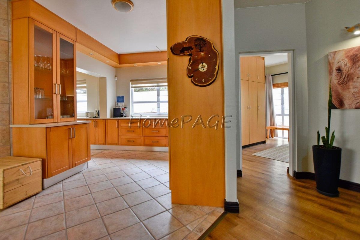 A view of a kitchen area with light wood cabinetry and tiled flooring, transitioning into a hallway with built-in cupboards and wood-look flooring.