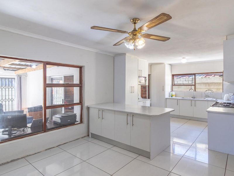 A functional kitchen featuring white cabinetry, a central island, tiled flooring, and a ceiling fan, with an internal window looking into an adjacent patio area.